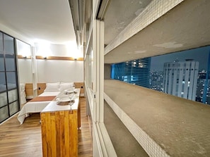 A modern hotel room with a large bed, a wooden side table, and a city view through a large window. - 2716B (São Paulo)
