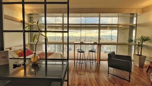 Een moderne woonkamer met uitzicht op de stad, een eethoek met krukken en een groot raam.