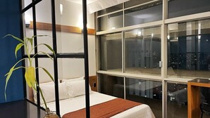 Een moderne slaapkamer met een groot raam, een bed met witte beddengoed en een houten vloer.