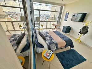 A modern bedroom with a city view, a bed, a desk, and a TV. - 3012B (São Paulo)