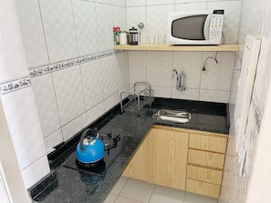 A compact kitchen with a microwave, kettle, and sink.