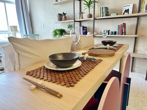 Ein Esstisch mit einer Schüssel, Stäbchen und einer Tischmatte. Im Hintergrund steht ein Bücherregal mit Büchern und Dekoration.