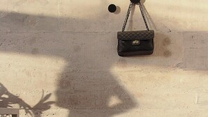 Ein Zimmer mit einer Betonwand, einer hängenden schwarzen Handtasche und einem rollbaren Koffer auf dem Boden.
