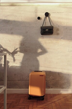 A room with a concrete wall, a hanging black handbag, and a wheeled suitcase on the floor. - 3217B (São Paulo)