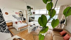 Ein modernes Wohnzimmer mit Sofa, Essbereich und Bett. Ein großes Fenster bietet Blick auf die Stadt.
