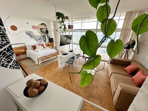A modern living room with a sofa, a dining area, and a bed. There is a large window providing a view of the city. - 3217B (São Paulo)
