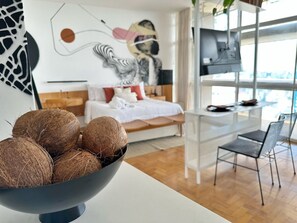 A modern bedroom with a bed, a desk, and a chair. There is a bowl of coconuts on a table in the foreground. - 3217B (São Paulo)