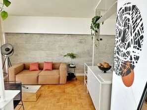 A modern living room with a herringbone wooden floor, a beige sofa with red cushions, a small side table with a plant, and a white radiator. - 3217B (São Paulo)