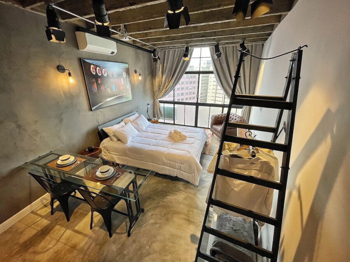 Een kamer met een bed, een tafel met borden, een ladder en een raam met gordijnen.