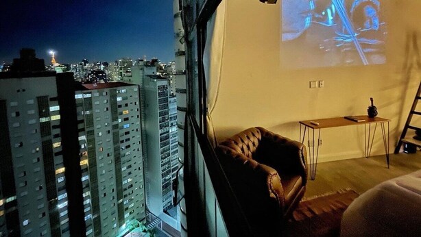 A room with a city view, a projector screen, a table, and a chair. - 2006B (São Paulo)