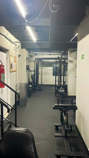 A gym with exercise equipment, a fire extinguisher, and a staircase. - 1902B (São Paulo)