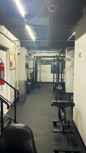 Ein Fitnessraum mit Trainingsgeräten, einem Feuerlöscher und einer Treppe.