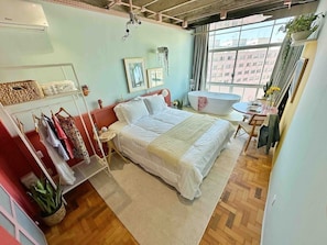 Ein Schlafzimmer mit Bett, Schminktisch, Fenster und einer Pflanze.