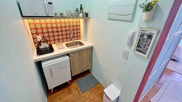 A compact kitchen with a dishwasher, a coffee machine, and a sink. There is a small refrigerator, a potted plant, and a framed picture on the wall. - 2002B (São Paulo)