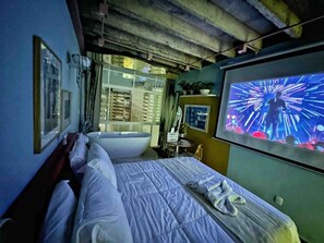 A hotel room with a bed, a large window, a sink, and a television screen displaying a colorful image. - 2002B (São Paulo)