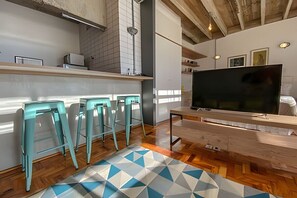 A modern kitchen with a large TV, bar stools, and a geometric patterned rug. - 1817B (São Paulo)