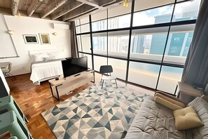 A modern living room with a large window, a sofa, a TV, and a patterned rug. - 1817B (São Paulo)