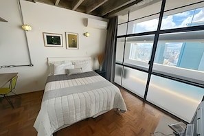 Ein Schlafzimmer mit großem Fenster, einem Bett, einem Schreibtisch und einem Stuhl.