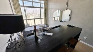 Una habitación moderna con un ventanal grande, una mesa negra con una botella de vino y copas, una lámpara y un espejo en la pared.