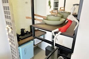 Eine kleine Küche mit einem blauen Schrank, einer Arbeitsfläche mit Wasserkocher, Topf und Holzlöffel.