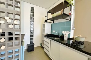 A modern kitchen with white cabinets, a black countertop, and a blue backsplash. There is a sink, a stove, and a small trash bin. - 2813B (São Paulo)