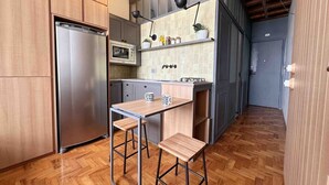 A compact kitchen with a built-in microwave, a stainless steel refrigerator, and a small dining table with two stools. - 3101B (São Paulo)