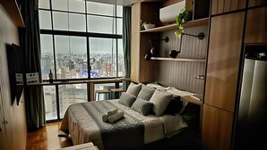A bedroom with a large window, a bed, a desk, and a wardrobe. - 3101B (São Paulo)