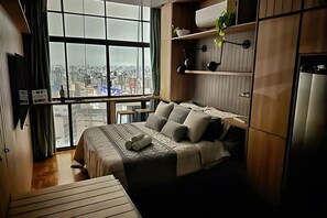 Ein Schlafzimmer mit großem Fenster, einem Bett, einem Schreibtisch und einem Kleiderschrank.