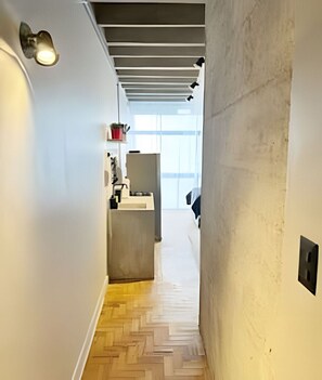 A hallway with a herringbone wooden floor, a kitchen area with a countertop and cabinets, and a window providing natural light. - 0813B (São Paulo)