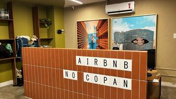 A reception area with a wooden partition displaying 'AIRBNB NO COPAN' and two framed pictures on the wall.