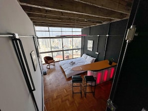 A bedroom with a bed, a desk, two chairs, and a window with a city view. - 2609B (São Paulo)