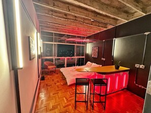 Une pièce avec un lit, une petite table et une chaise. Il y a une fenêtre qui offre une vue sur la ville la nuit.