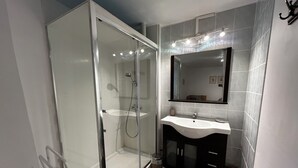 Une salle de bain moderne avec une douche à parois de verre, un lavabo blanc et un meuble-lavabo aux tons foncés.