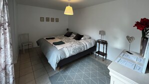 Une chambre à coucher comprenant un lit, une chaise, une table de chevet avec une lampe, et une étagère murale agrémentée d’objets décoratifs.