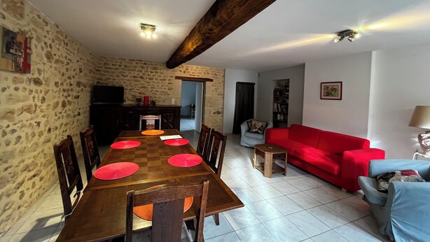 Un coin repas avec une table et des chaises en bois, un canapé rouge et un mur en pierre.