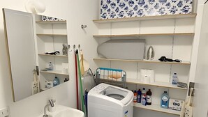 Ein Badezimmer mit Waschbecken, Spiegel, Ablagen für Pflegeprodukte und einer Waschmaschine.