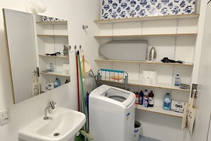 Ein Badezimmer mit Waschbecken, Spiegel, Ablagen für Pflegeprodukte und einer Waschmaschine.