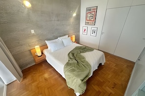 A bedroom with a bed, bedside lamps, a wall clock, and a wardrobe.