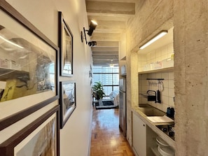A hallway with framed artwork, a kitchen area with a sink and cabinets, and a staircase leading to an upper level. - 1207B (São Paulo)