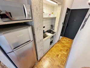 A compact kitchen with a microwave, a refrigerator, and a stove. - 1207B (São Paulo)