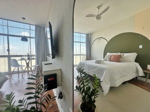 A hotel room with a bed, a desk, a chair, a plant, and a large window. - 2606B (São Paulo)