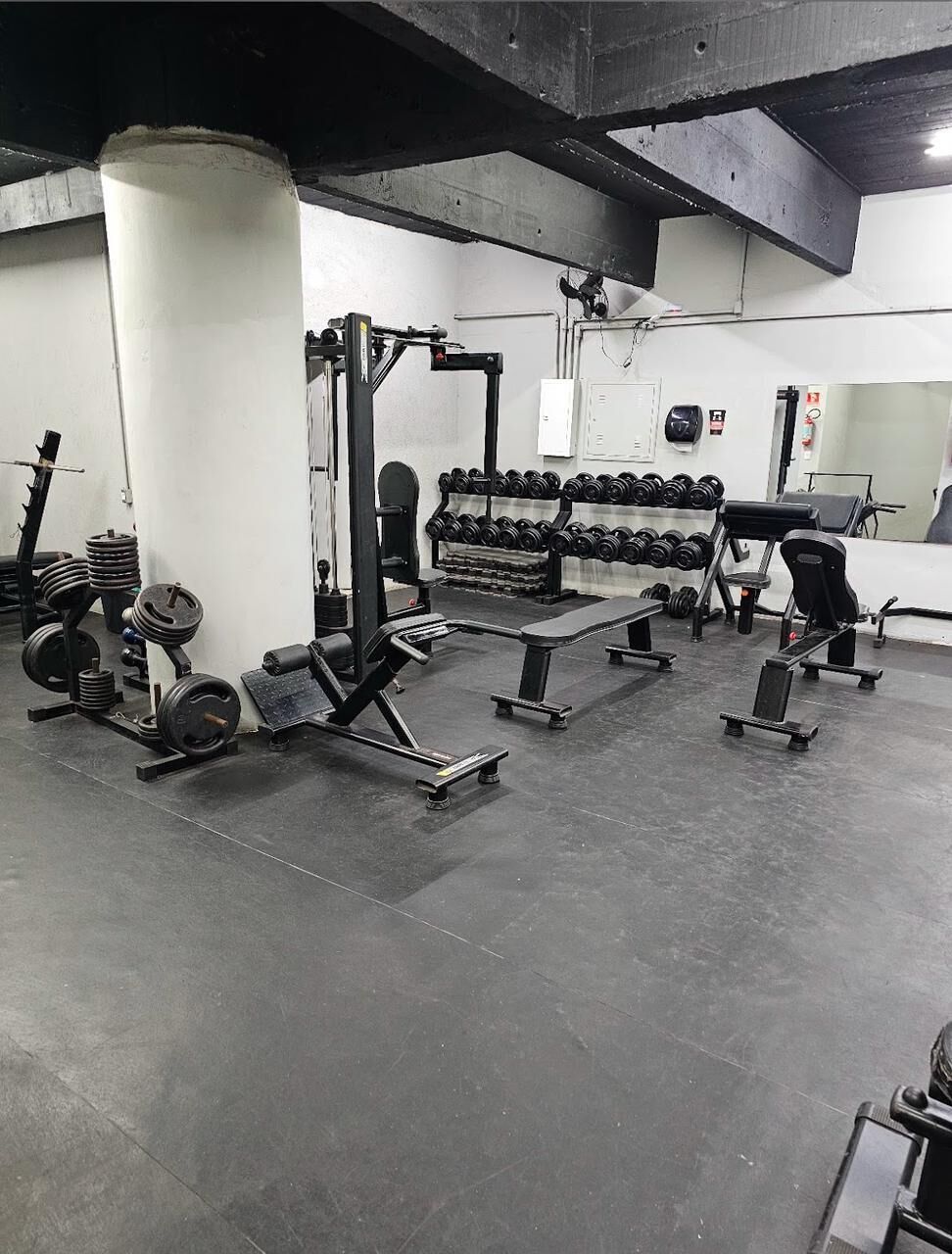 Uma academia com equipamentos de musculação, bancos e halteres.