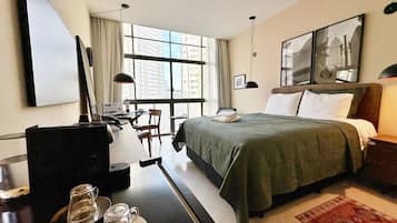 A hotel room with a bed, a desk with a computer, a coffee machine, and a window with a city view.
