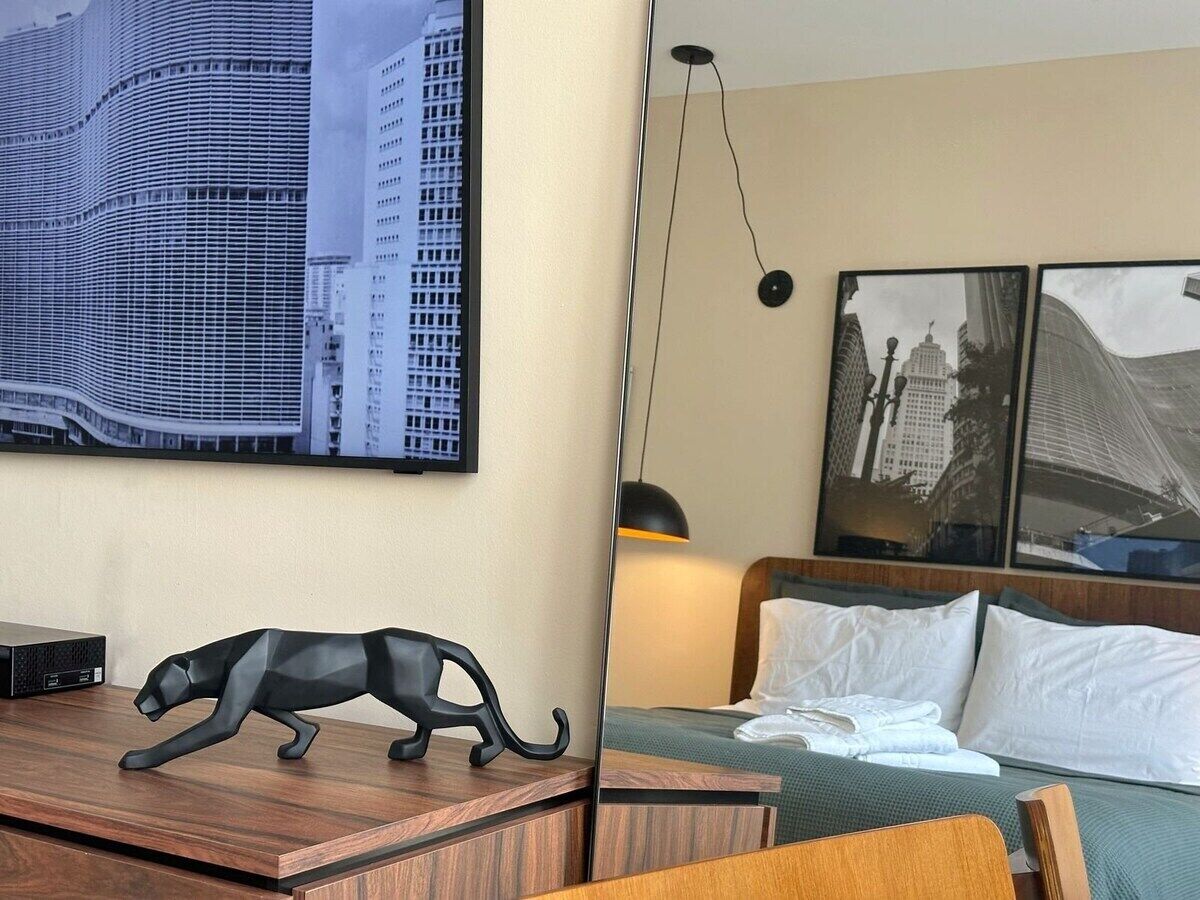 Une chambre d’hôtel avec un lit, un bureau, un téléviseur fixé au mur et une grande fenêtre.