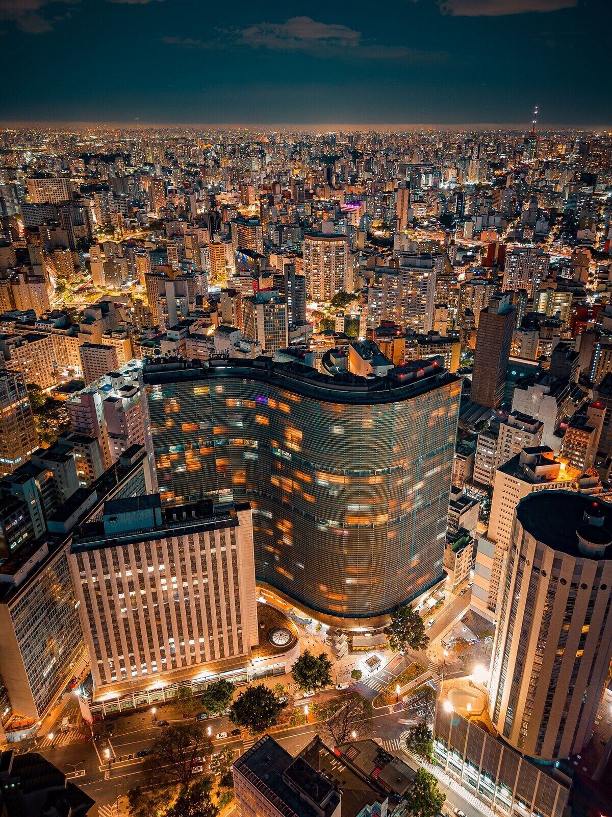 A high-rise building with a curved facade, surrounded by a dense urban environment with other high-rise buildings.