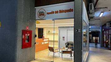 A hotel entrance with a reception desk, a fire alarm, and a glass door leading inside.