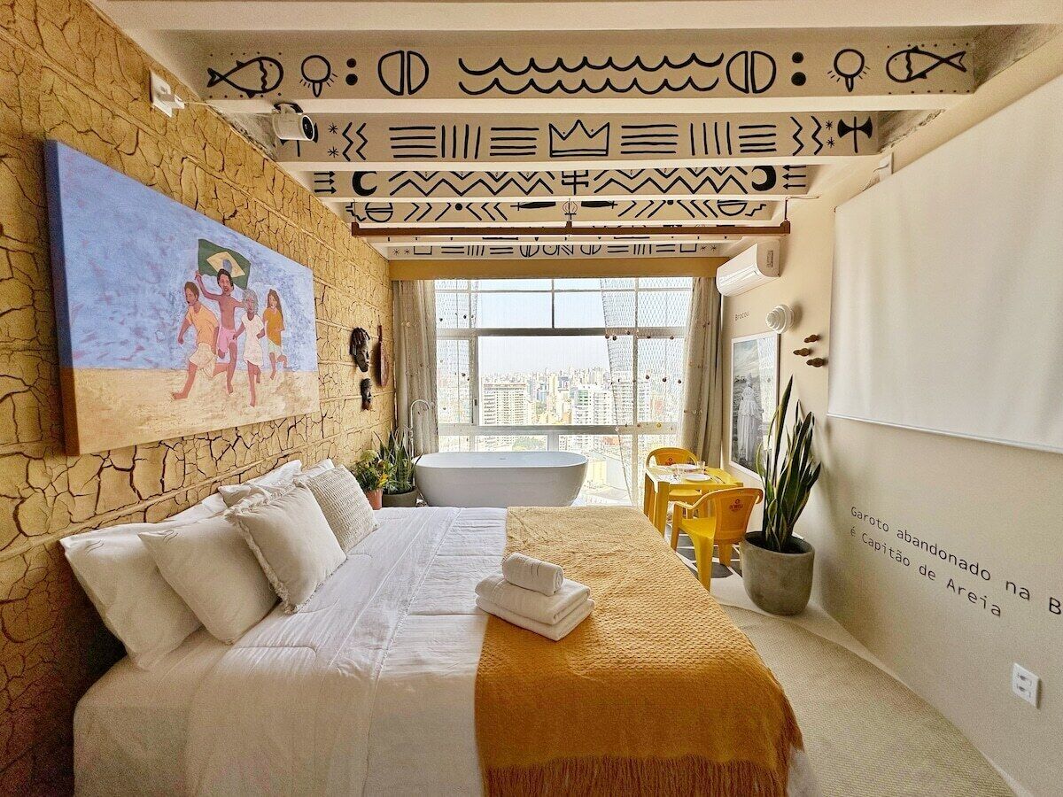 Ein Schlafzimmer mit einem Bett, einem Gemälde, einer Badewanne und Blick auf die Stadt.