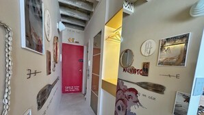 Un couloir orné d’œuvres d’art, avec une porte rouge et un miroir fixé au mur.