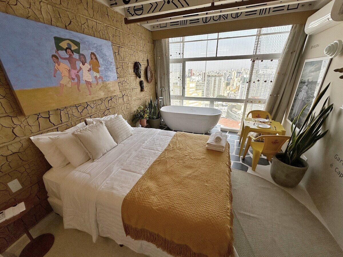 Ein Hotelzimmer mit einem großen Bett, einer Badewanne, einem Essbereich und Blick auf die Stadt.