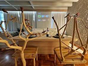 A dining area with a wooden table and chairs, a projector screen in the background, and a window with curtains. - 2315B (São Paulo)